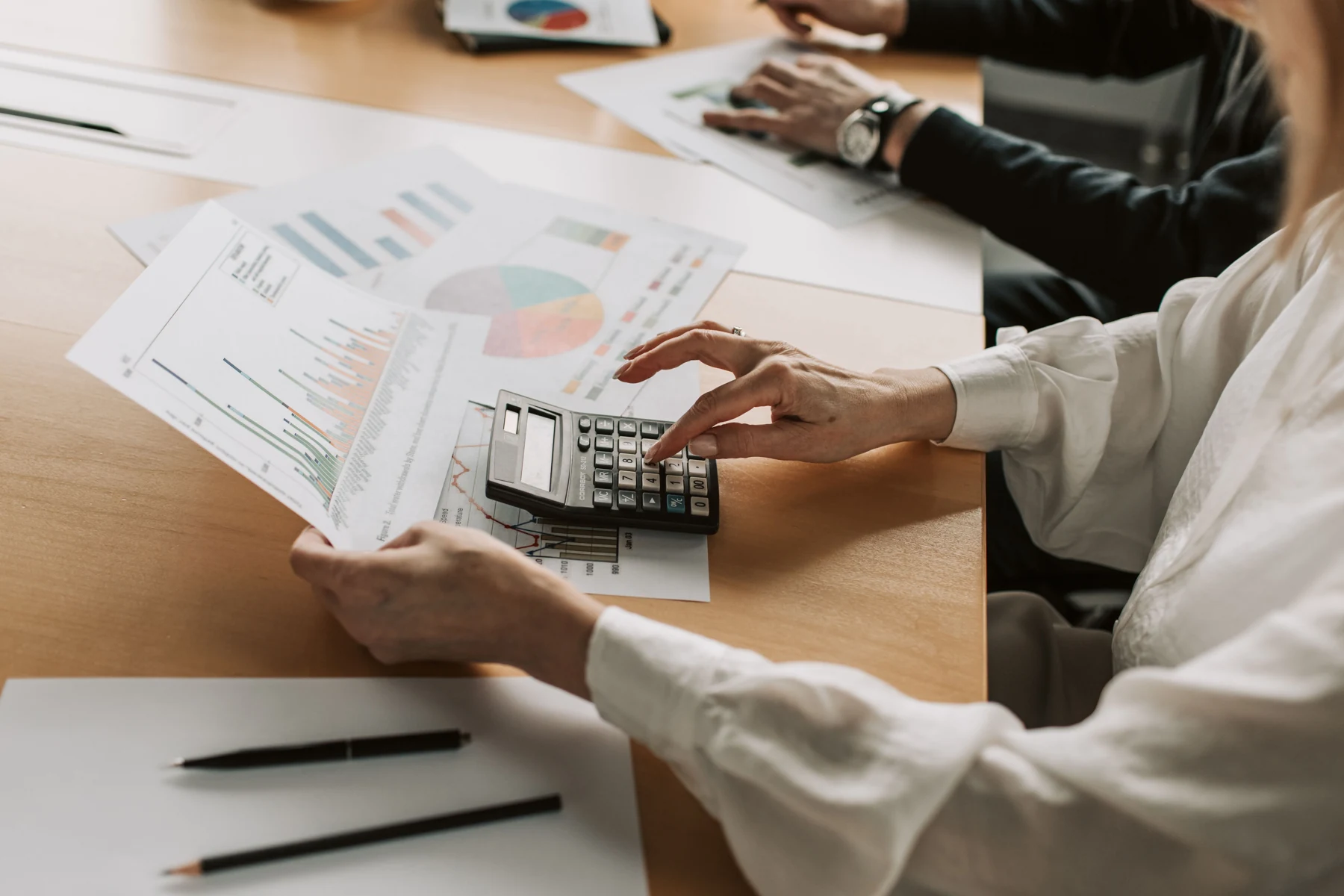 Hands use a calculator while reviewing printed business reports with charts.